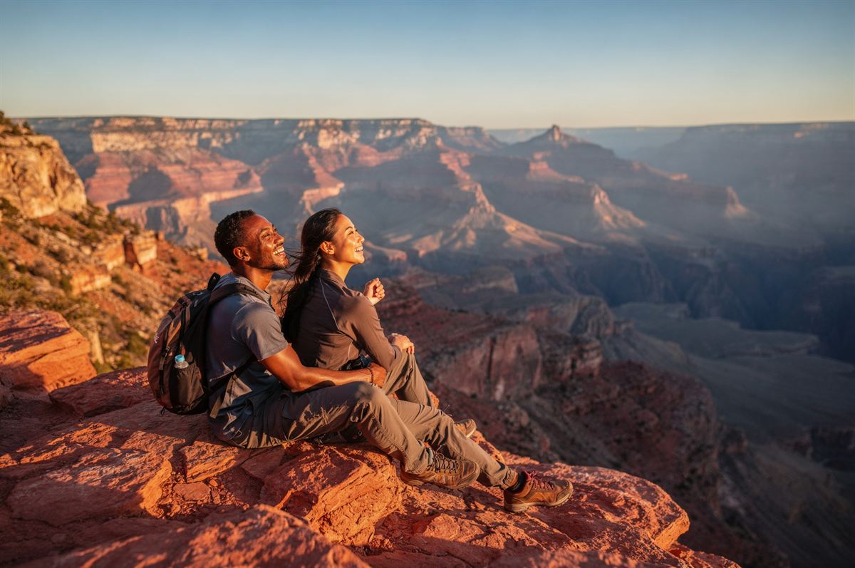 A couple sitting together on a rock ledge overlooking the Grand Canyon at sunset.